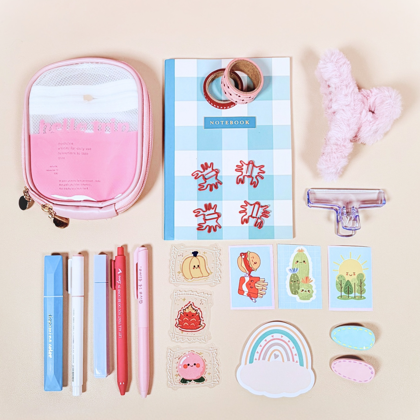 Stationery items including a pink pouch, notebook, pens, and stickers on a beige background